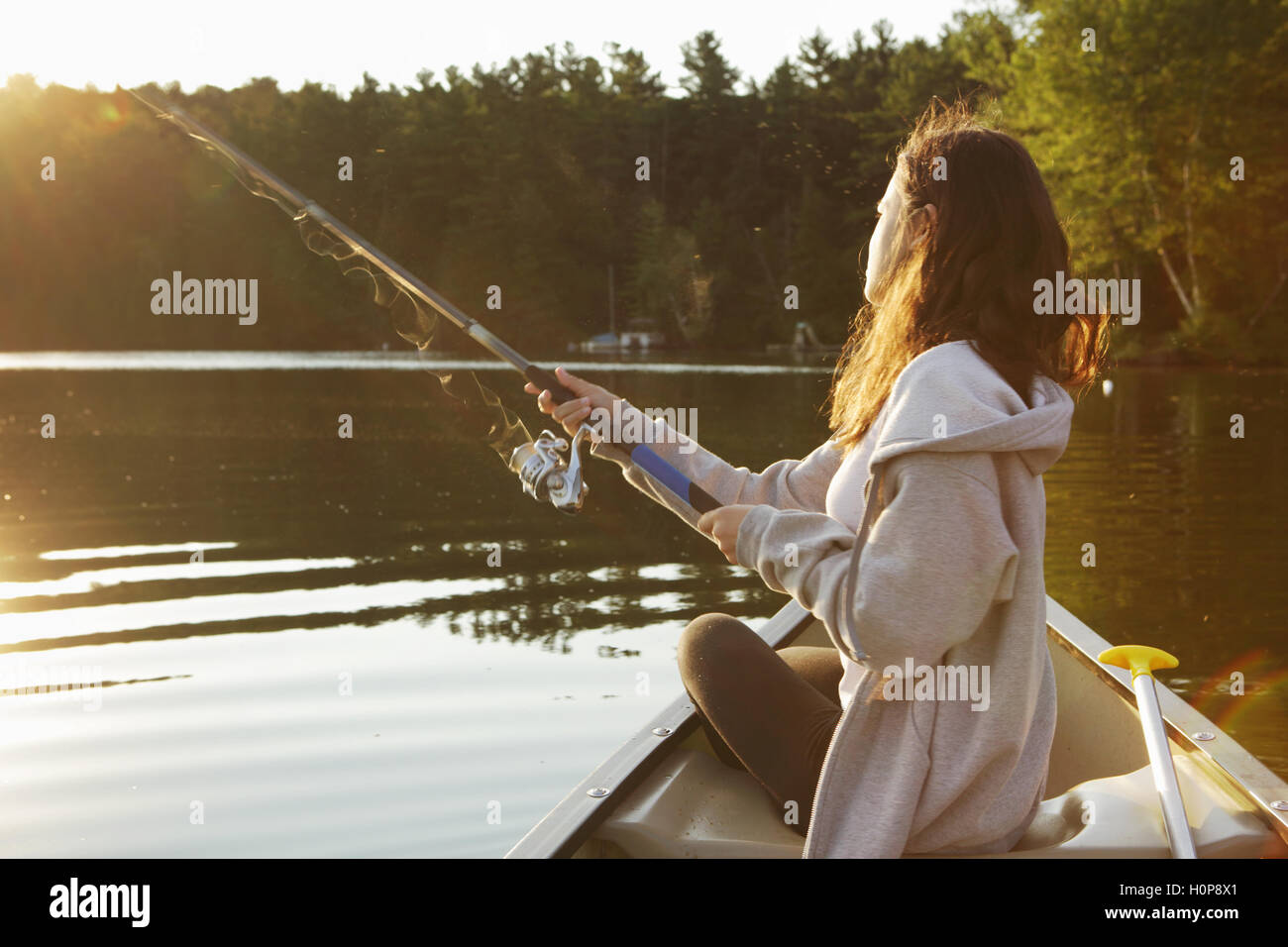 Ragazza con canna da pesca a bordo di una canoa su un lago nel Vermont come il sole che sorge Foto Stock