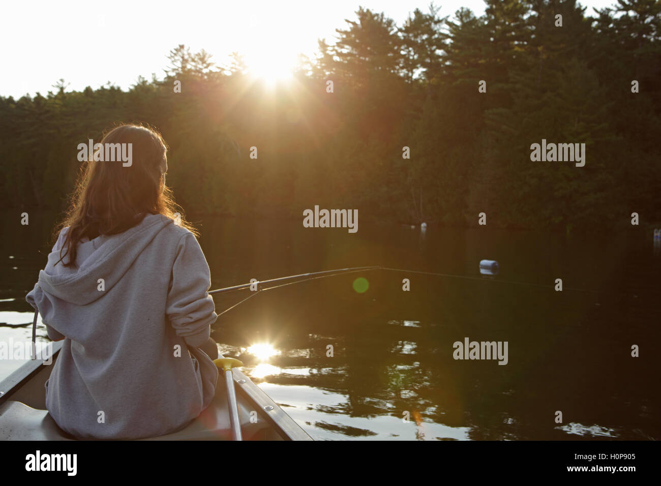 Ragazza con canna da pesca a bordo di una canoa su un lago nel Vermont come il sole che sorge Foto Stock