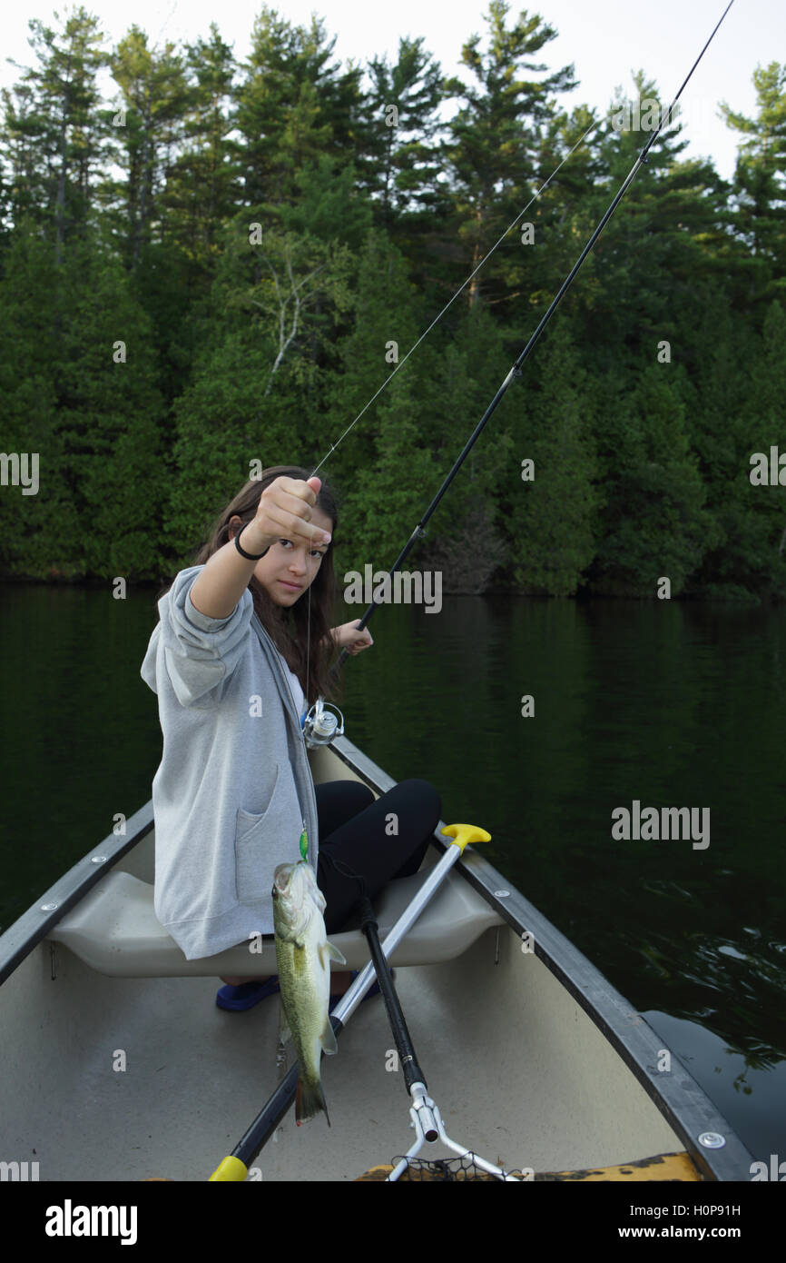 Ragazza la pesca la cattura di un bass da una canoa su un lago nel Vermont Foto Stock