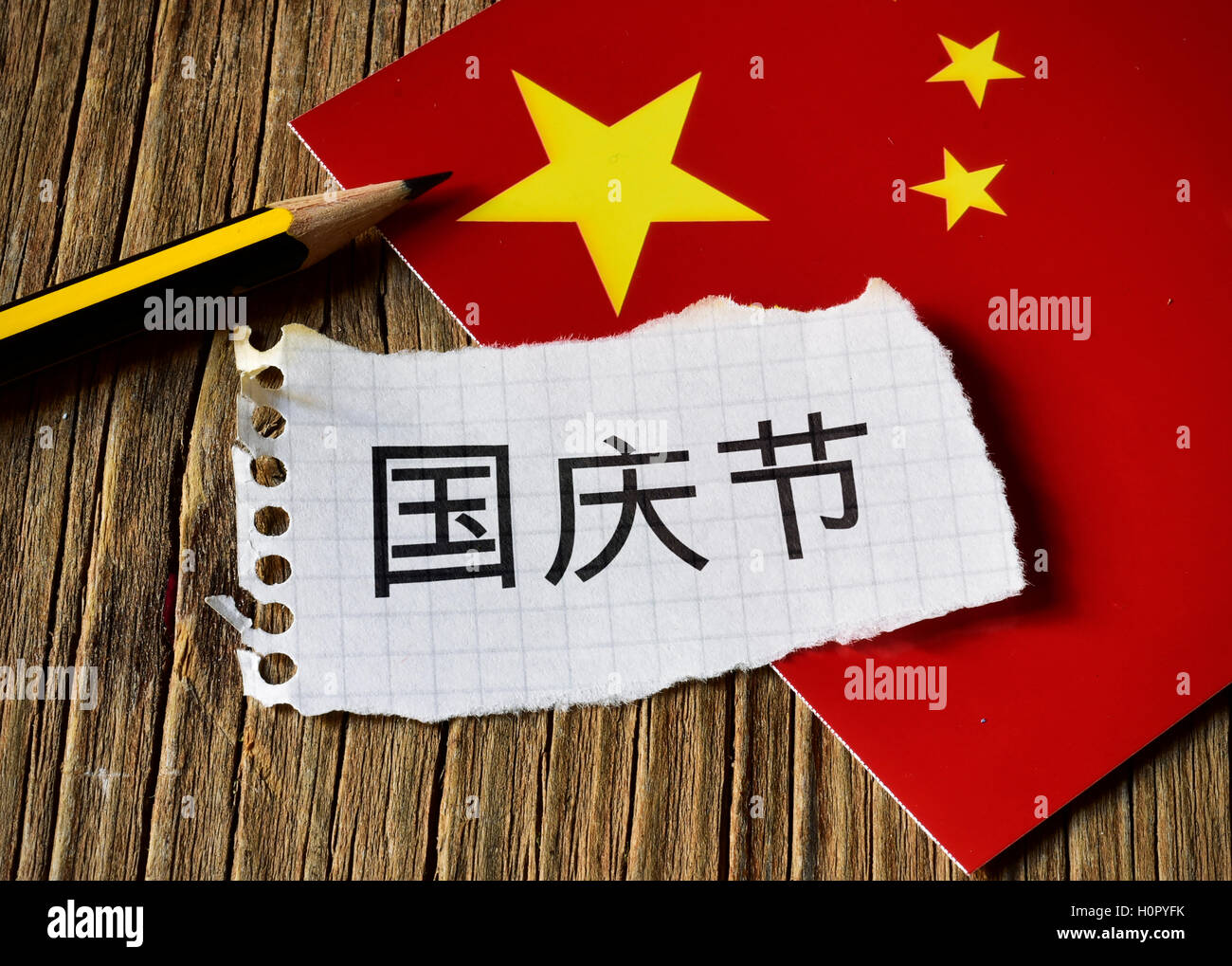 Primo piano di una pace della carta con il testo Giornata Nazionale scritta in cinese, una matita e la bandiera della Cina, posto su un rustico wo Foto Stock