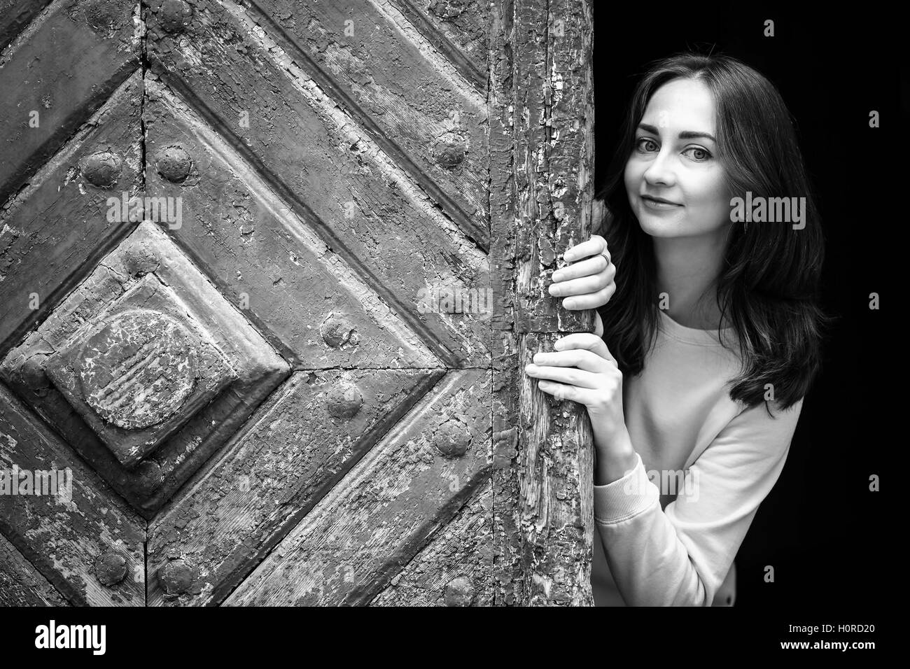 Ragazza giovane e carina del peering da dietro l antica porta di legno, in bianco e nero photo. Foto Stock