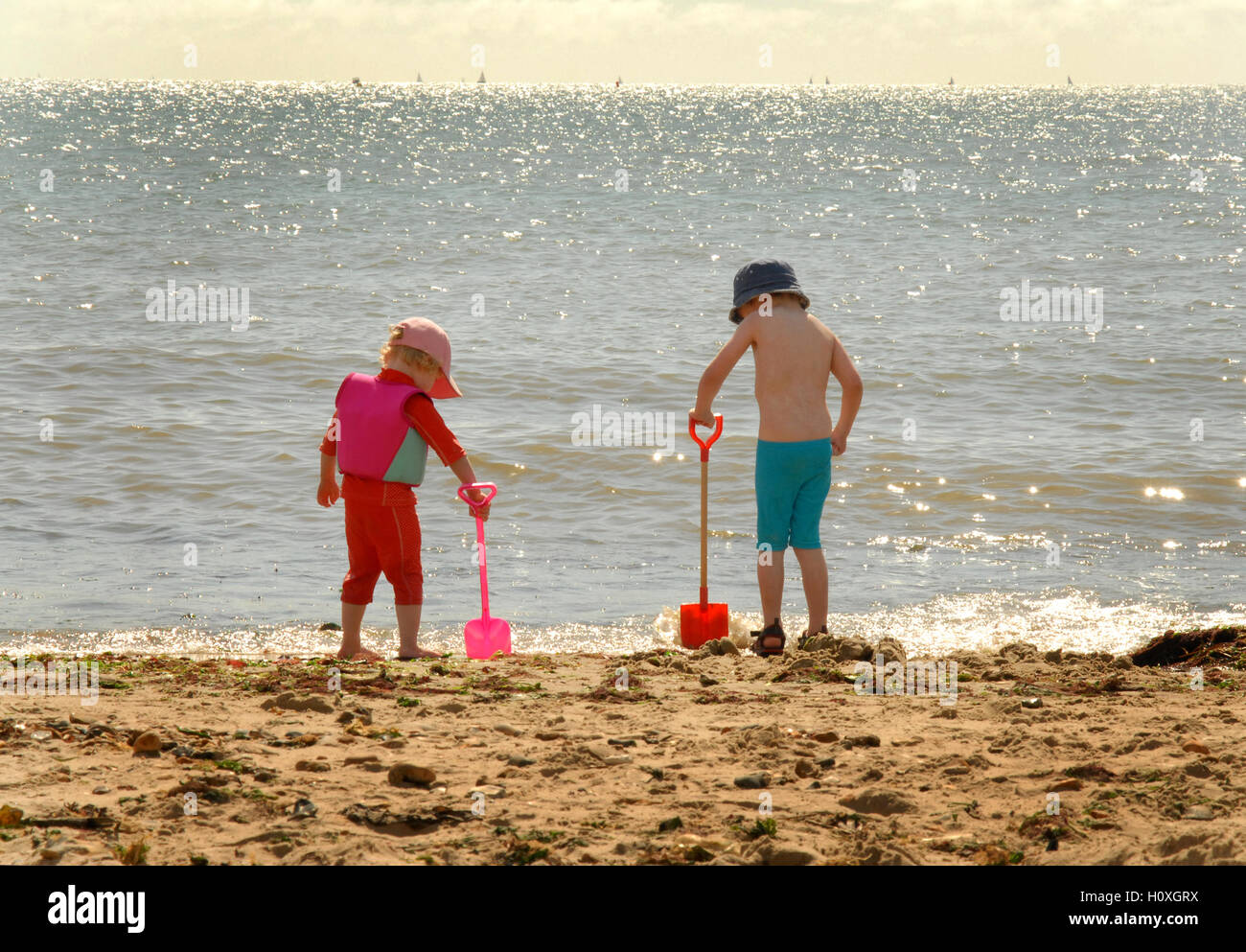 Sabbia, mare e picche - due giovani figli guardare come le onde lavare fino contro la loro picche. Foto Stock