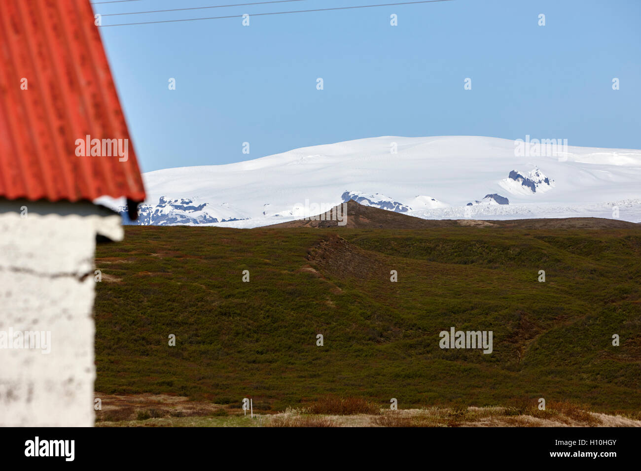 Dipinto di rosso metallo ondulato tetto su una farm annesso in Islanda con vista di katla e ghiacciaio myrdalsjokull Foto Stock