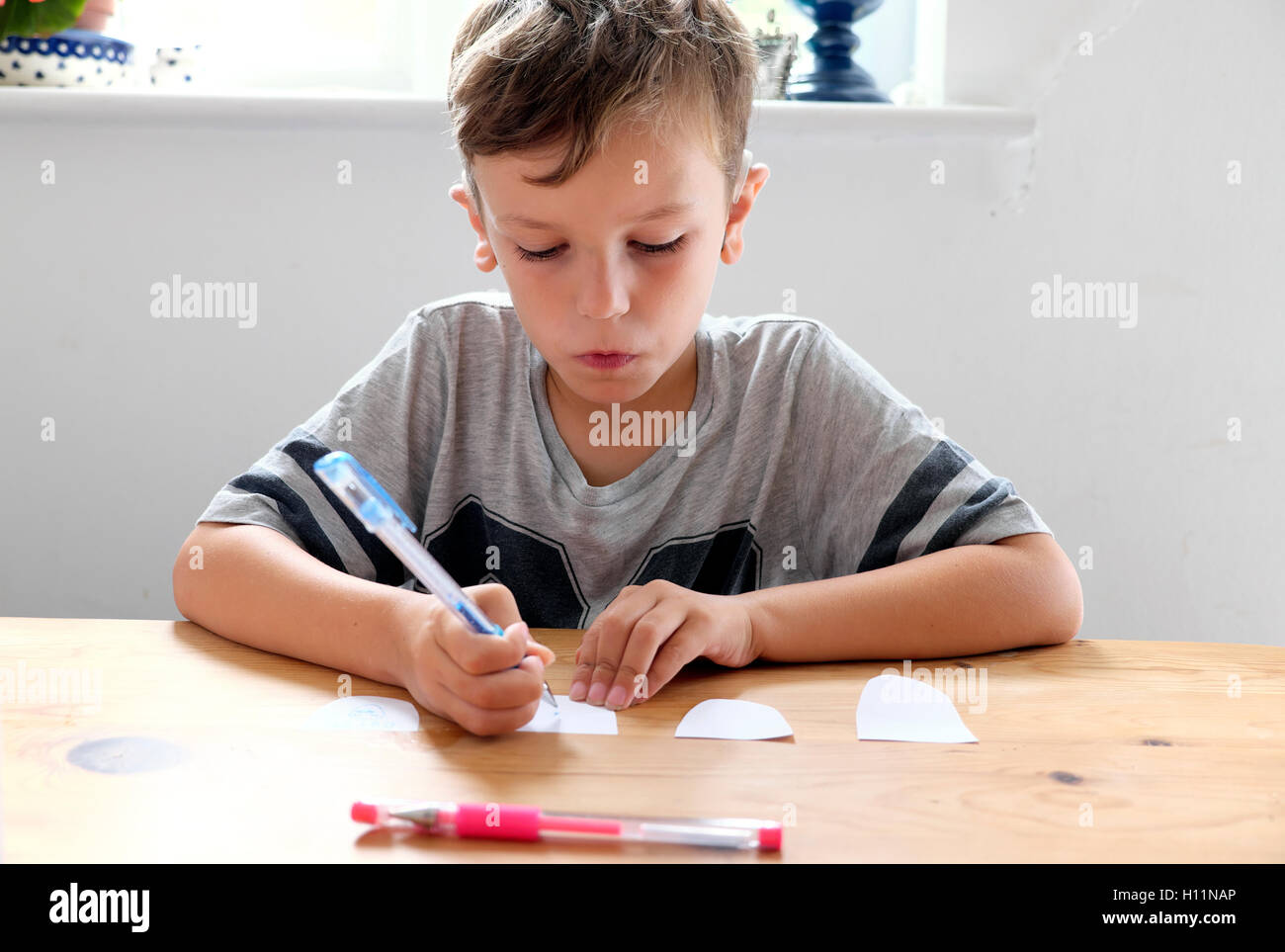 Giovane ragazzo pensieroso 6 bambino a casa seduto da solo a un tavolo disegno schizzo su pezzo di carta con penna in Gran Bretagna UK. KATHY DEWITT Foto Stock