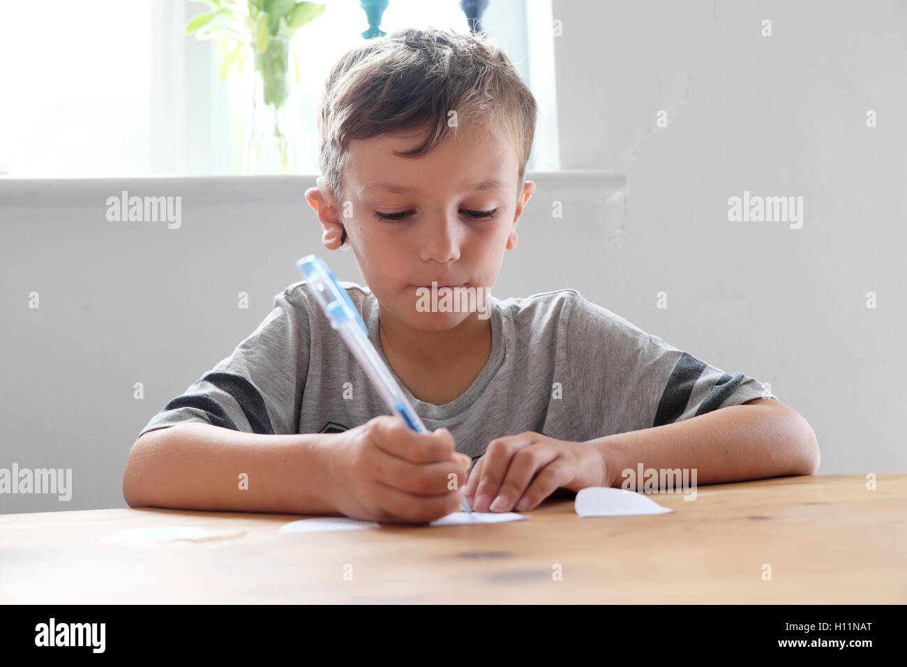 Giovane ragazzo pensieroso 6 bambino a casa seduto da solo a un tavolo disegno schizzo su pezzo di carta con penna in Gran Bretagna UK. KATHY DEWITT Foto Stock