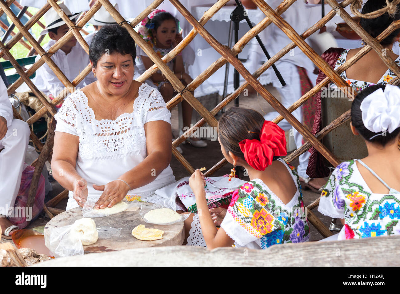 Una donna e i suoi figli la preparazione del mais masa per rendere la tortilla a Hanal Pixan altare contest di Merida in Messico. Foto Stock