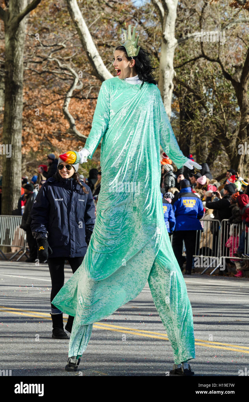 Un stiltwalker vestita come la Statua della Libertà sorride alla folla guardando il Macy's Thanksgiving Day parade. Foto Stock