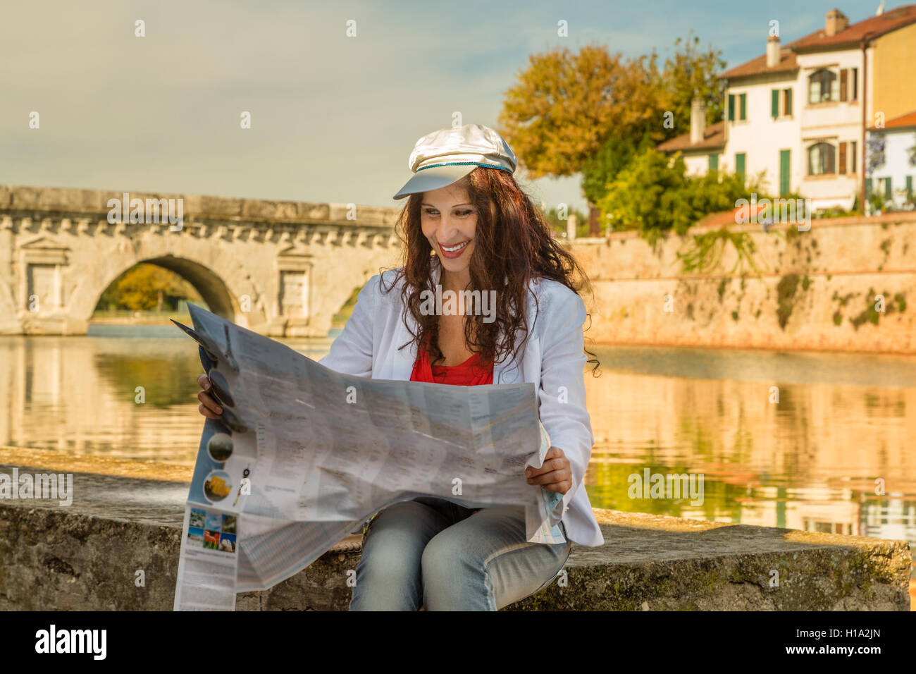 Rimini, Italia, donna consultando la mappa turistica con antico ponte romano in background Foto Stock