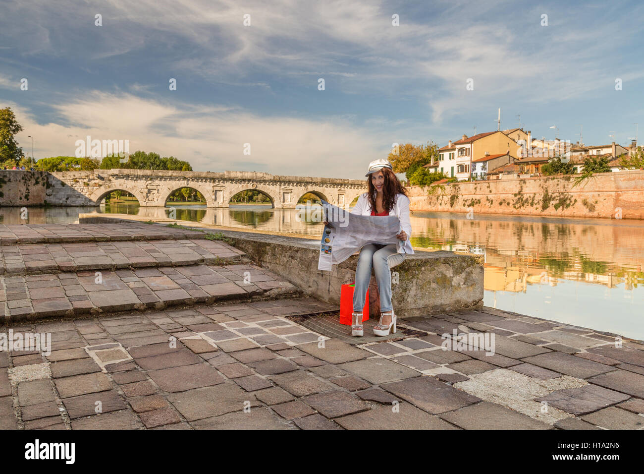 Rimini, Italia, donna consultando la mappa turistica con antico ponte romano in background Foto Stock