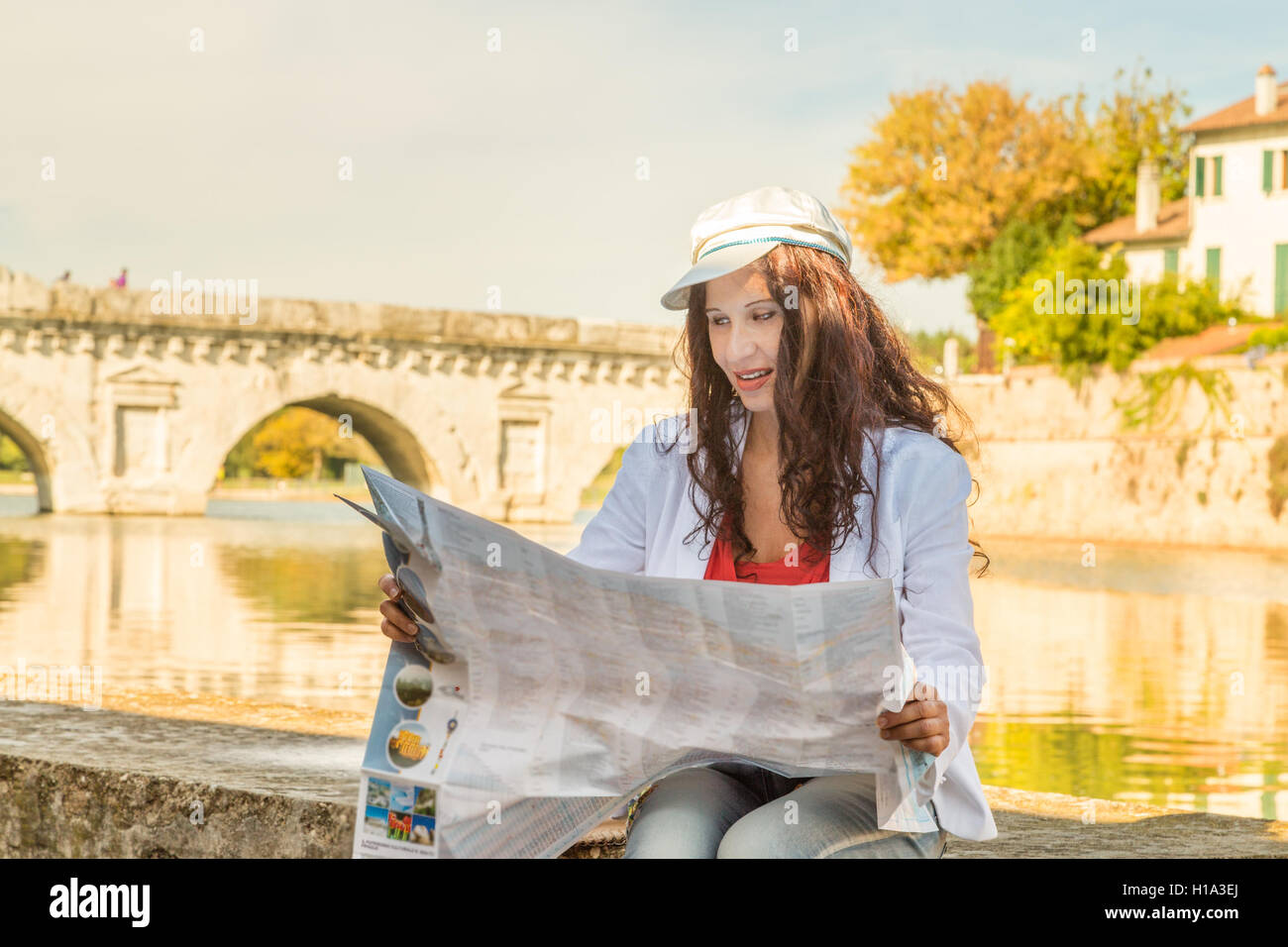 Rimini, Italia, donna consultando la mappa turistica con antico ponte romano in background Foto Stock