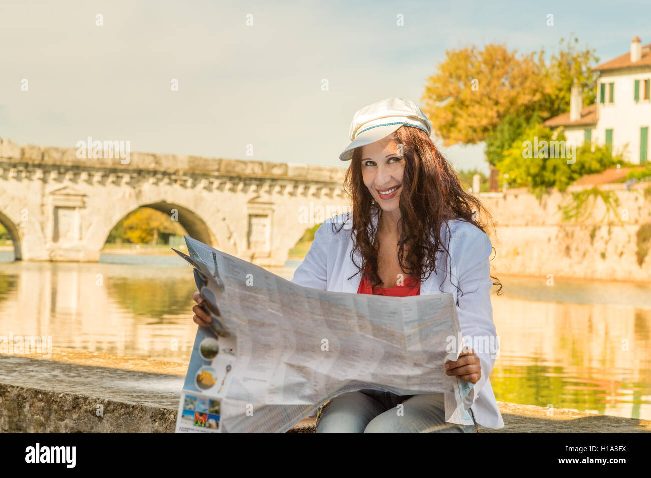 Rimini, Italia, donna consultando la mappa turistica con antico ponte romano in background Foto Stock