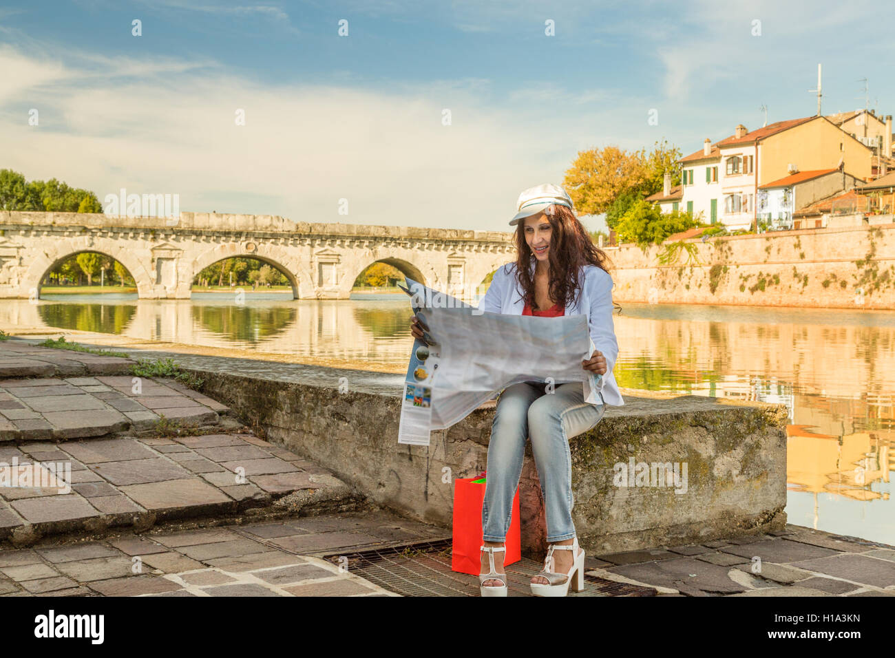Rimini, Italia, donna consultando la mappa turistica con antico ponte romano in background Foto Stock