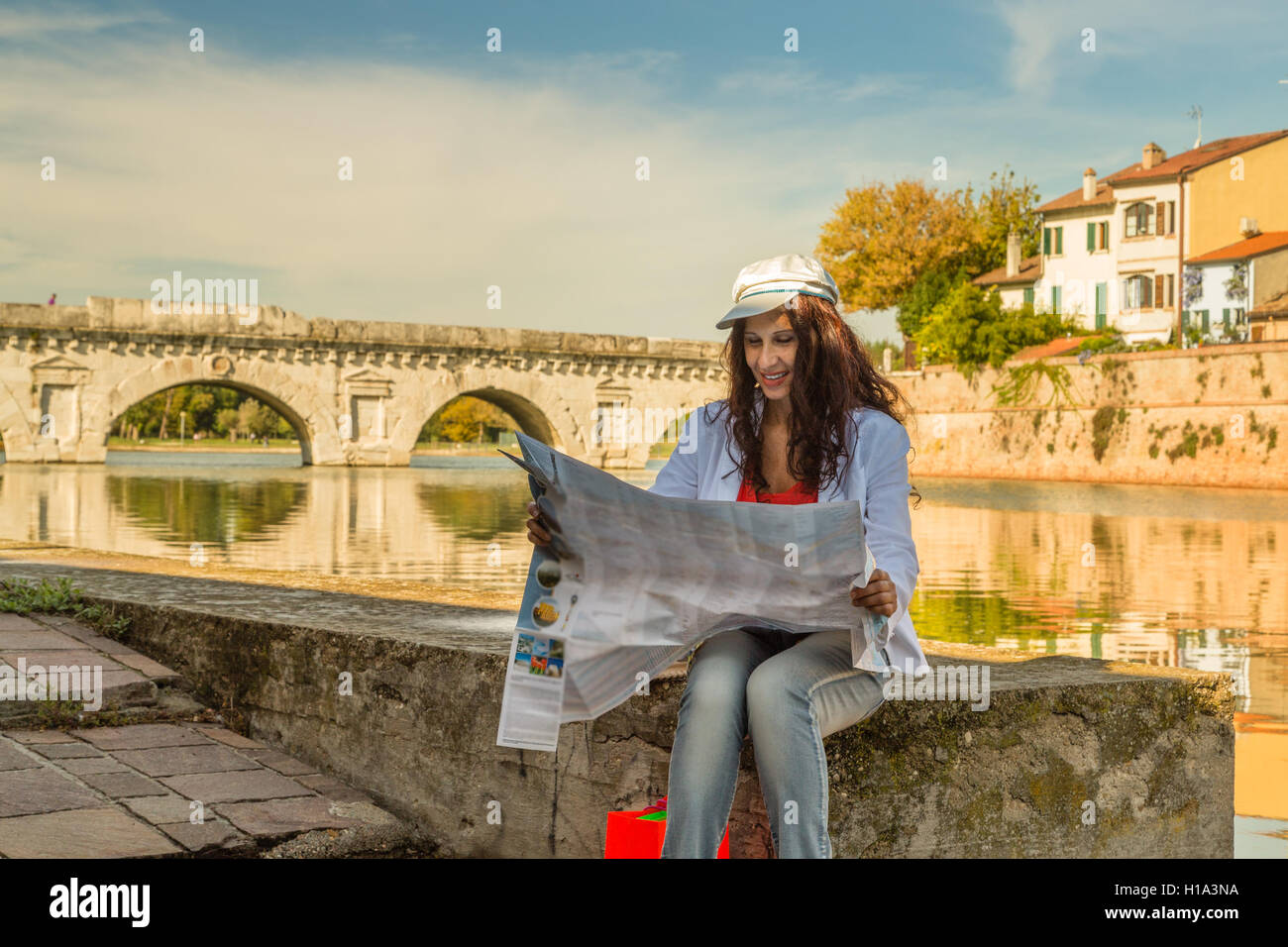 Rimini, Italia, donna consultando la mappa turistica con antico ponte romano in background Foto Stock
