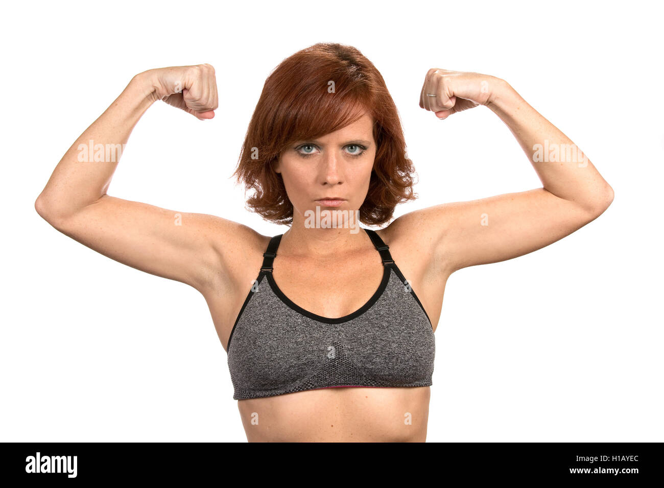 Sottile redheaded freckled donna si flette il suo bicipite muscoli indossando un reggiseno per lo sport. Foto Stock