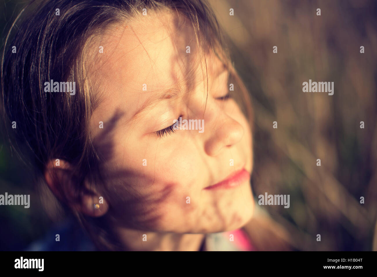 Faccia la ragazza con gli occhi chiusi sotto il sole di sera con erba ombre Foto Stock