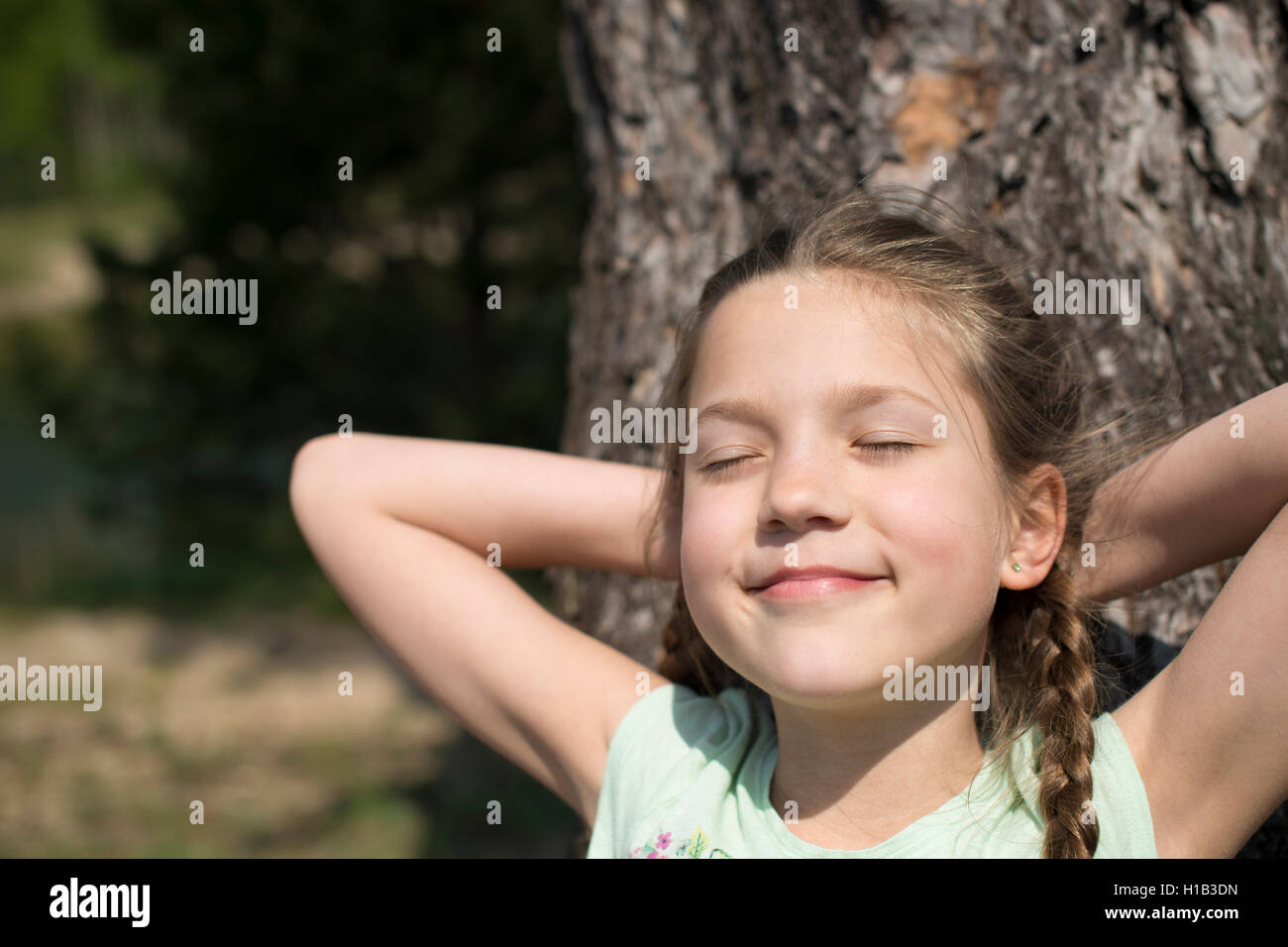 Bambino felice ragazza a prendere il sole con gli occhi chiusi vicino al grande albero Foto Stock