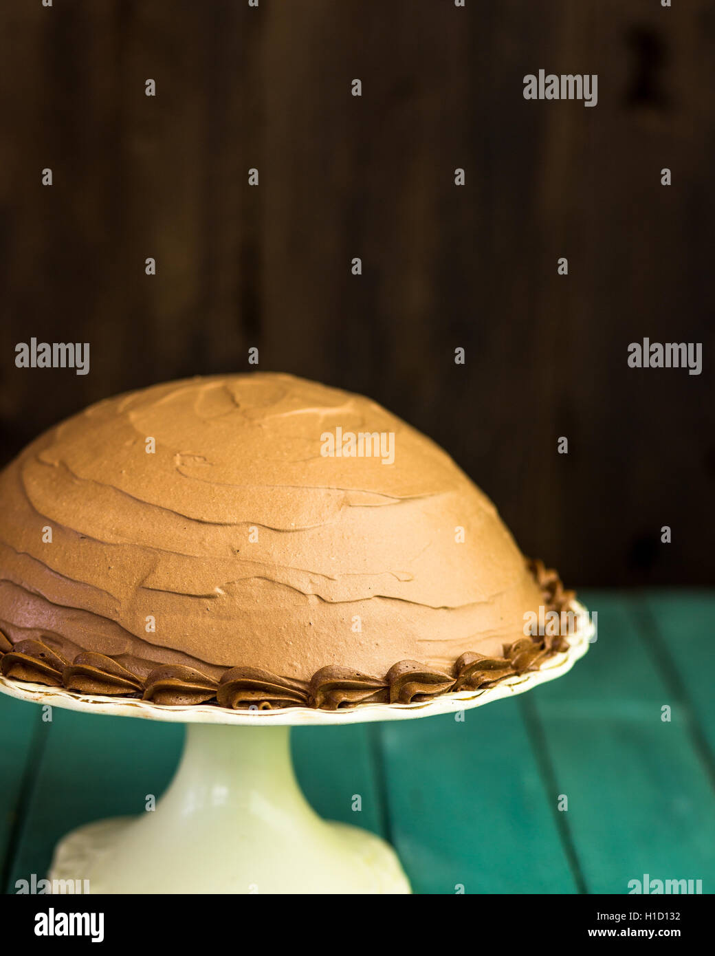Caffè al Cioccolato nocciola mezza sfera torta con tubazioni decorativo sulla torta bianca stand e scuro dello sfondo turchese Foto Stock