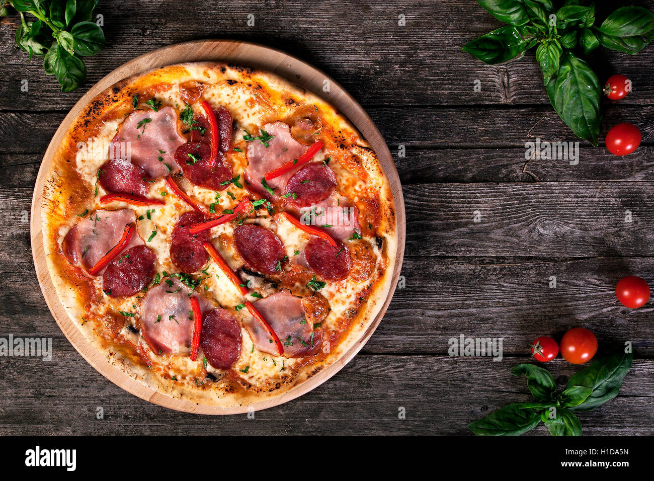 Freschi e deliziosi salsiccia per pizza pizza con salumi , bacon , pepe rosso, verde cipolle e formaggio sullo sfondo di legno. Vista dall'alto. Foto Stock