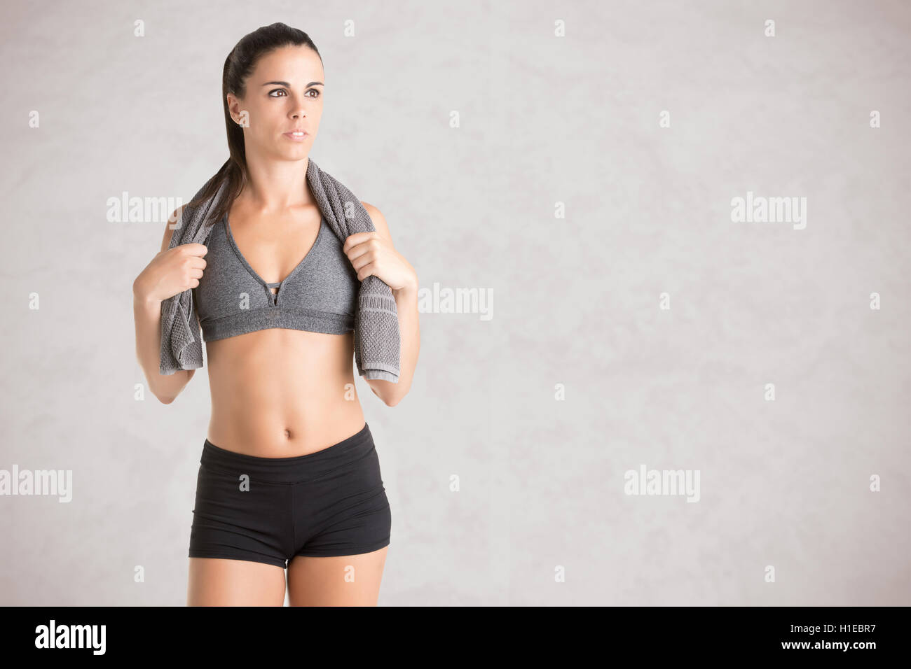 Donna in appoggio con un asciugamano attorno al collo dopo un allenamento fitness, isolato in grigio Foto Stock