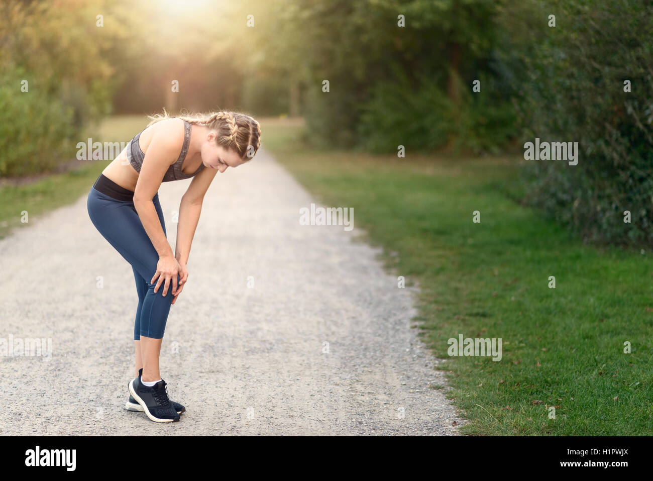 Giovane donna limbering up prima di partecipare al corso di formazione facendo esercizi di allungamento dei muscoli di lei su un paese percorso nella luce del mattino Foto Stock