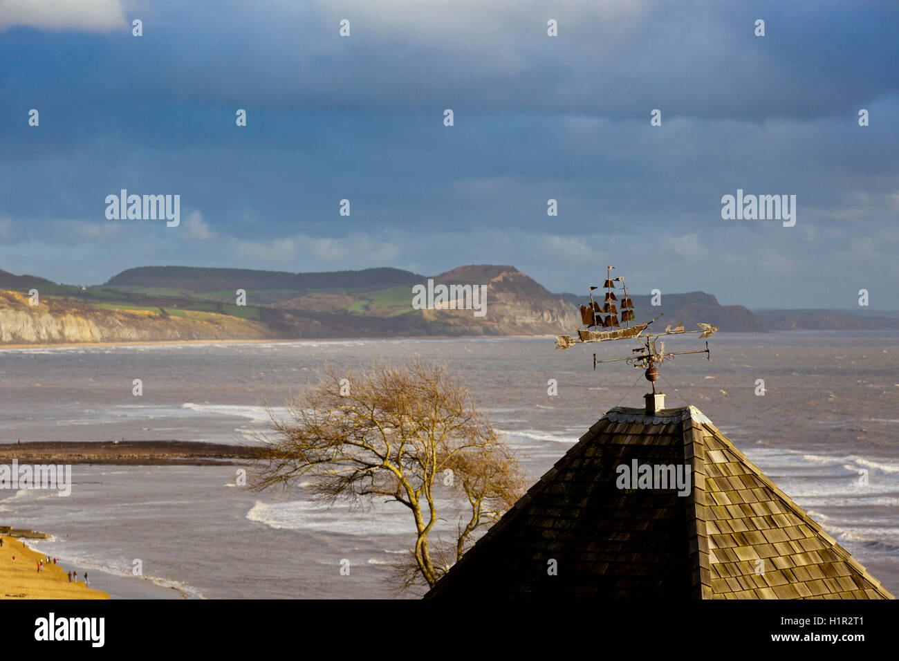 Un weathervane di un alto veliero a caccia di una balena su una casa a Lyme Regis con cappuccio dorato al di là, Dorset, England, Regno Unito Foto Stock