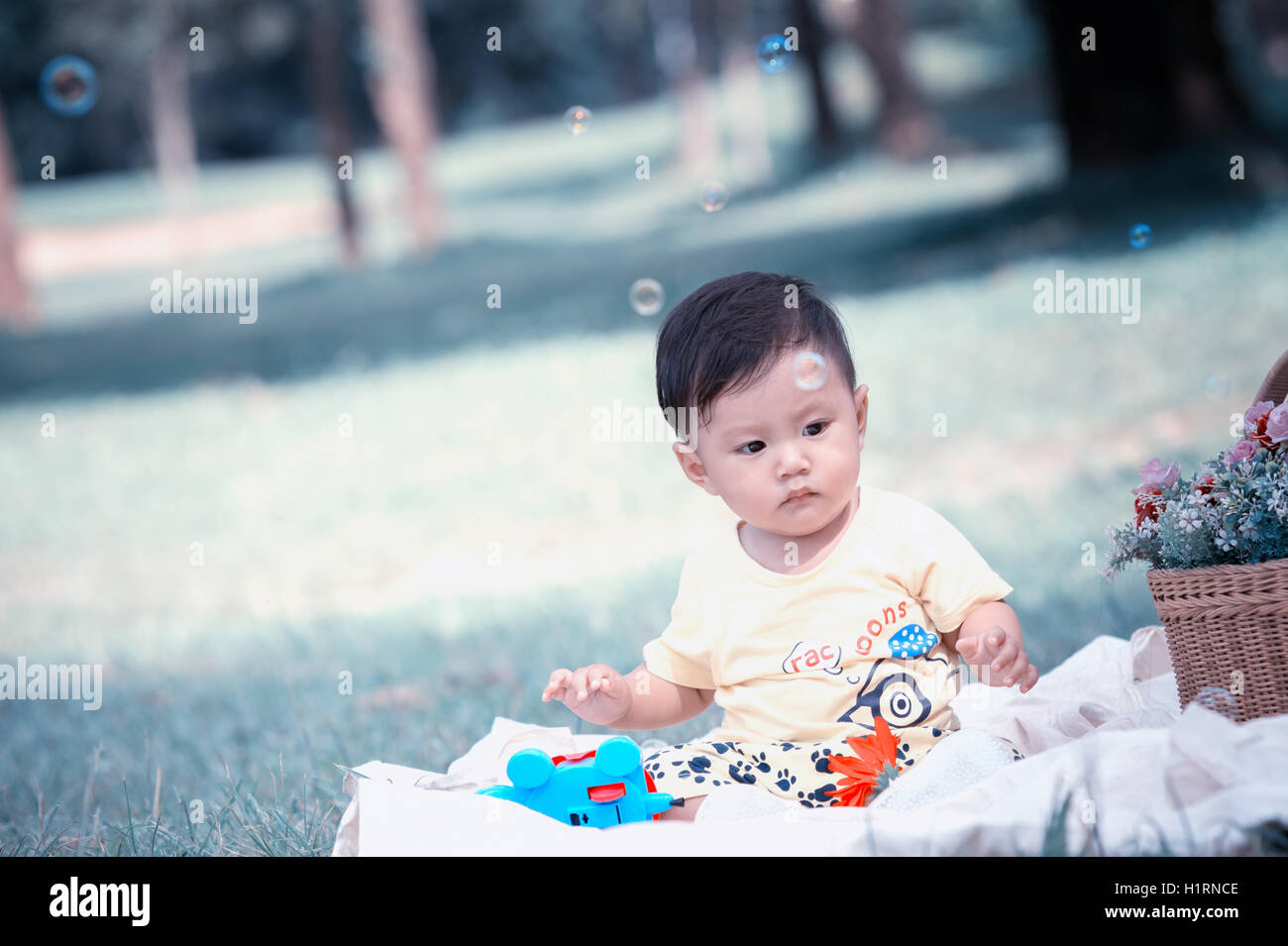 Asia bambino seduto sul prato verde nel parco con bolle di sapone Foto Stock