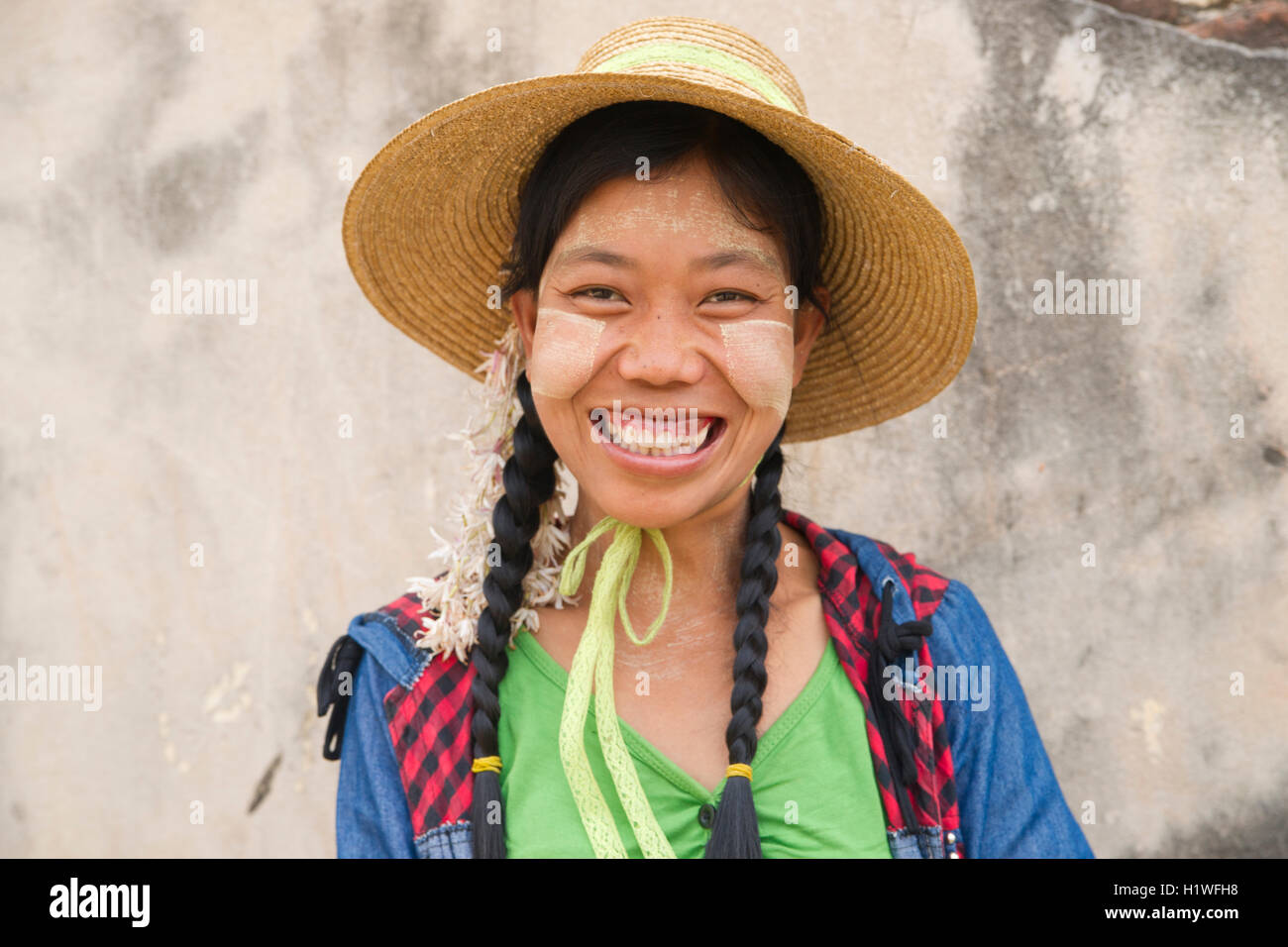 Sorridente Myanmar donna che indossa thanaka lozione per la pelle, con abiti colorati e cappello di paglia. Foto Stock