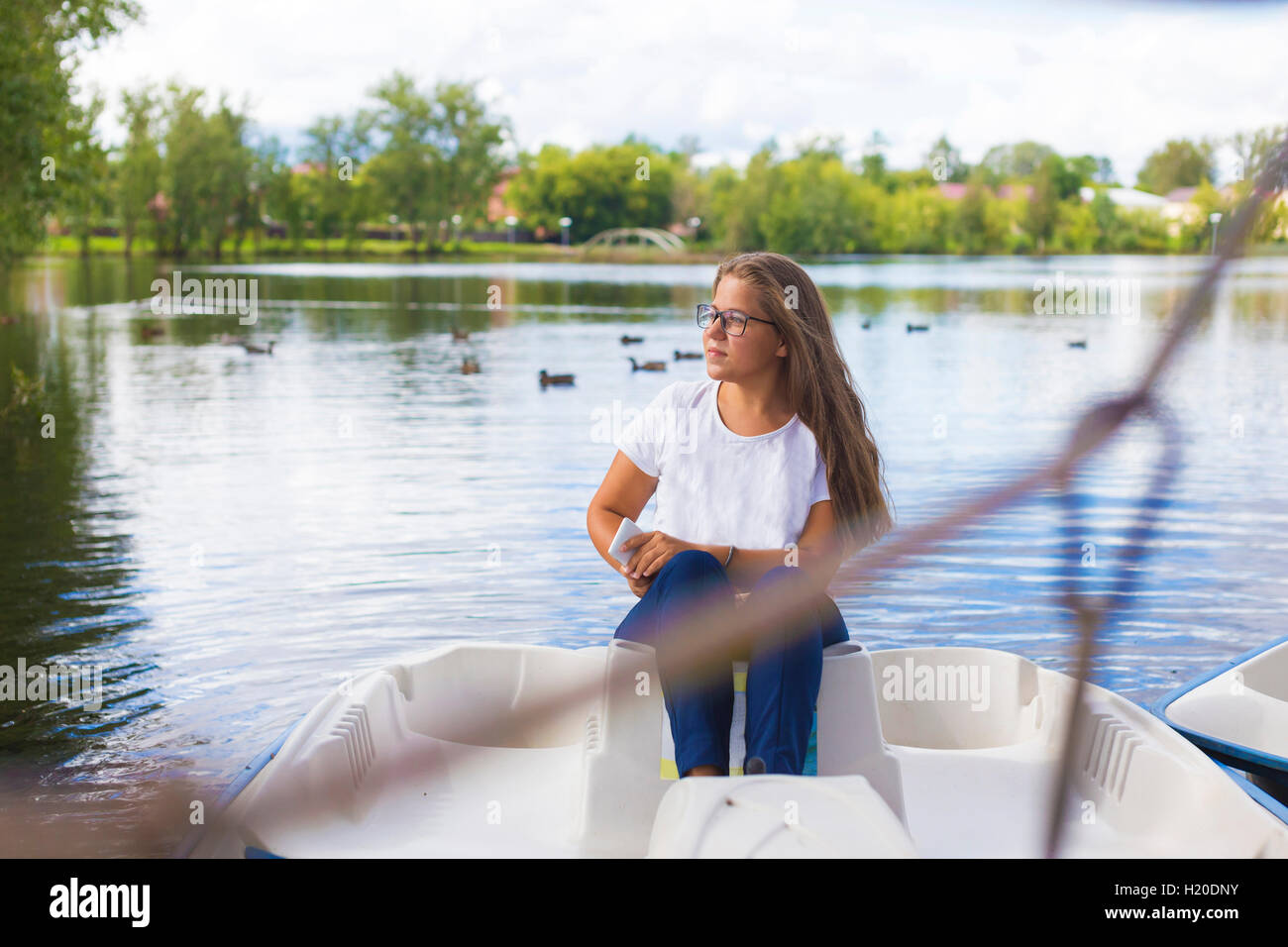Russia, Tikhvin, ragazza adolescente con lo smartphone, seduti in barca Foto Stock
