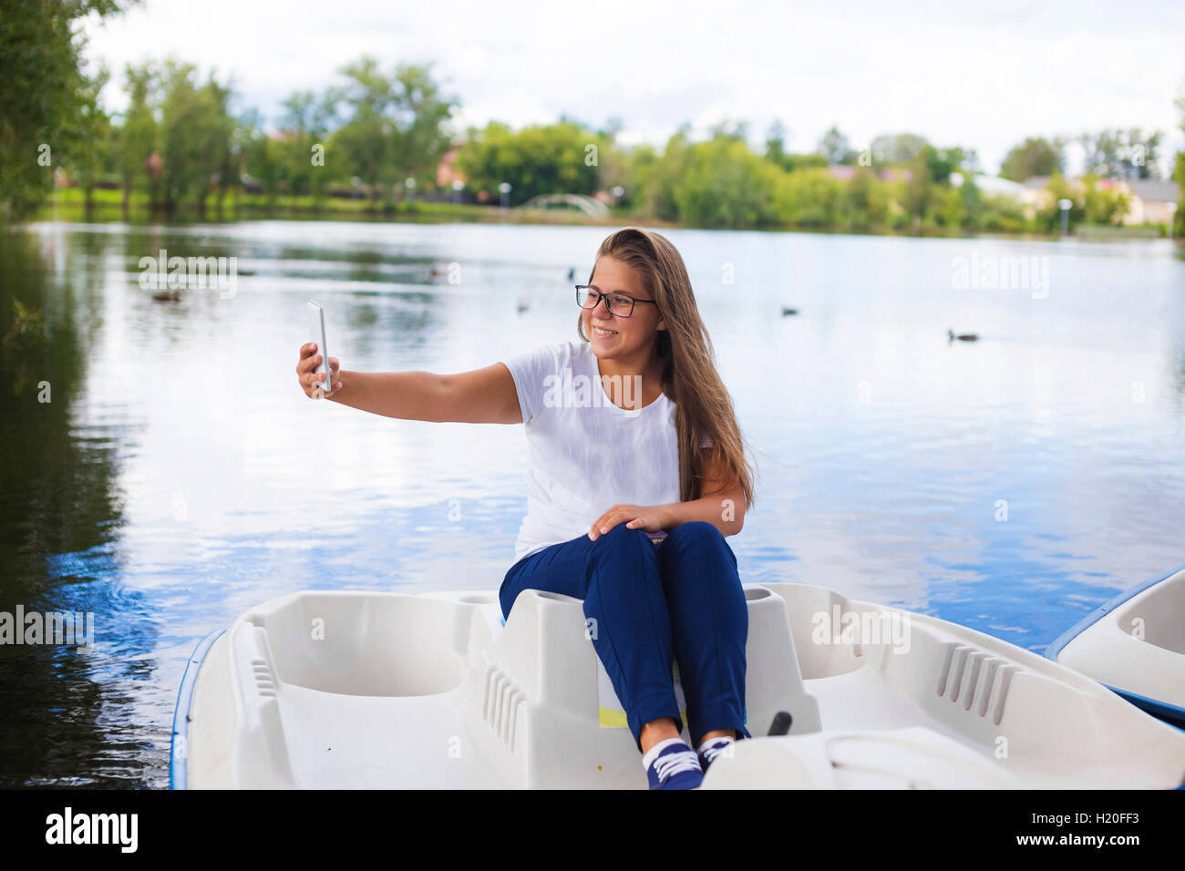Russia, Tikhvin, ragazza adolescente con lo smartphone, seduti in barca, selfie Foto Stock