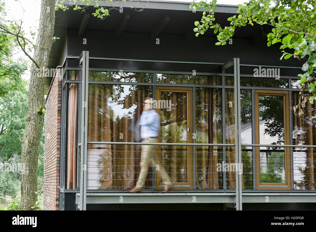 Uomo al telefono camminando sul balcone della sua casa Foto Stock