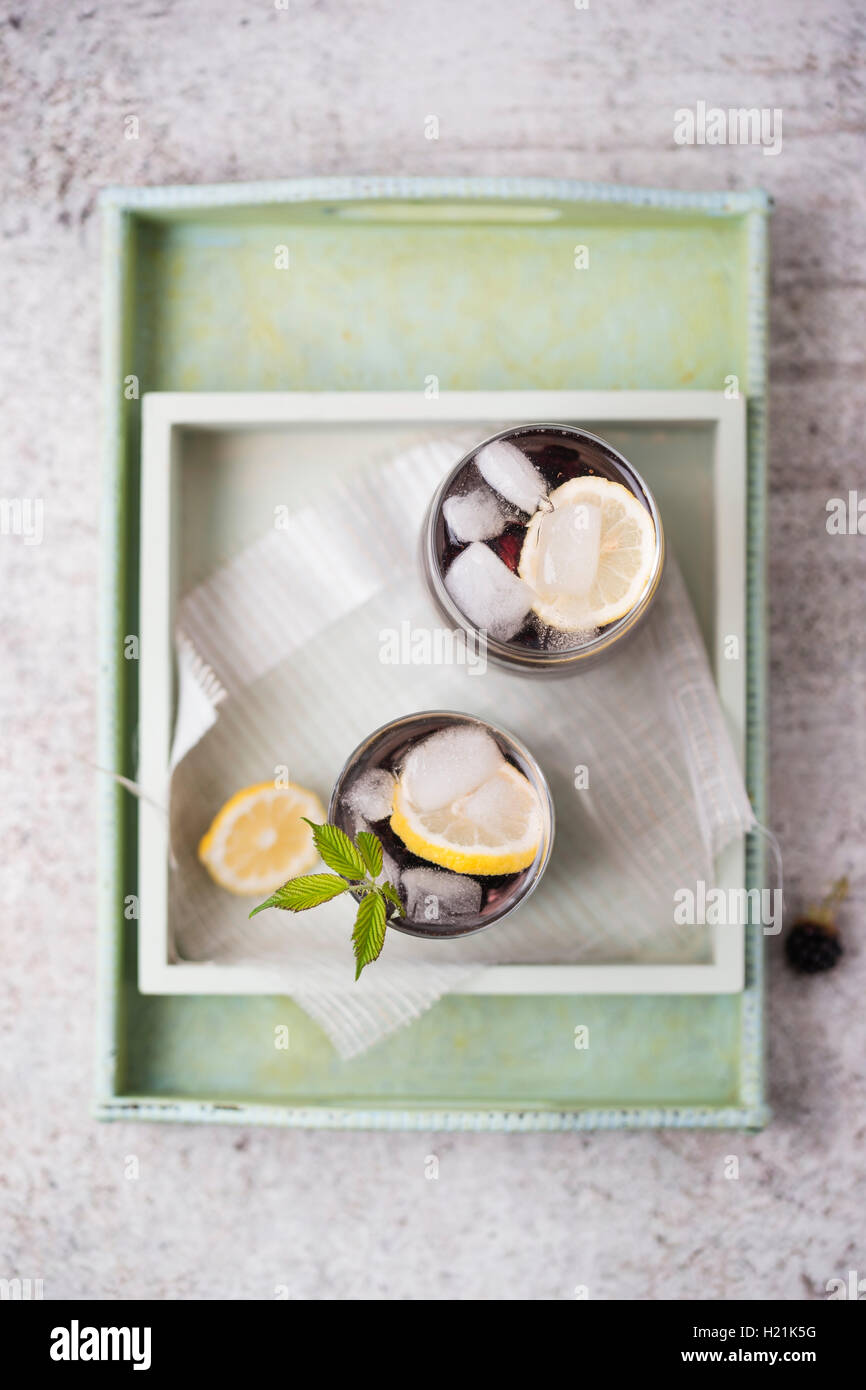Blackberry limonade con limone e cubetti di ghiaccio in bicchieri, sul vassoio Foto Stock