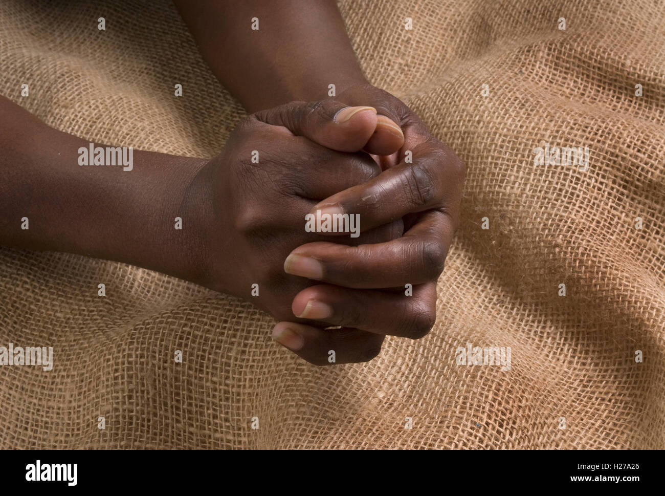 African mani giunte in preghiera su di un panno di Hesse sfondo. Foto Stock