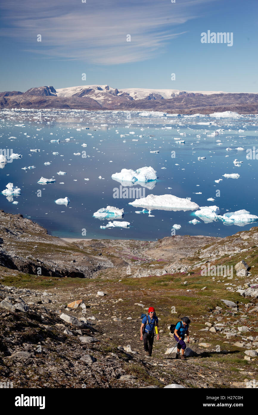 Gli escursionisti una salita sul bordo del fiordo di Sermilik vicino insediamento di Tiniteqilaq, Groenlandia icecap in distanza, est della Groenlandia Foto Stock