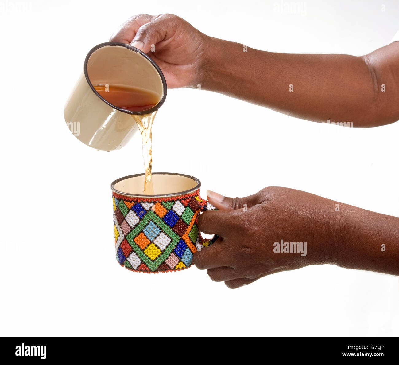 Mani africane che versano il tè da una tazza di stagno smaltata in un'altra tazza decorata. Foto Stock