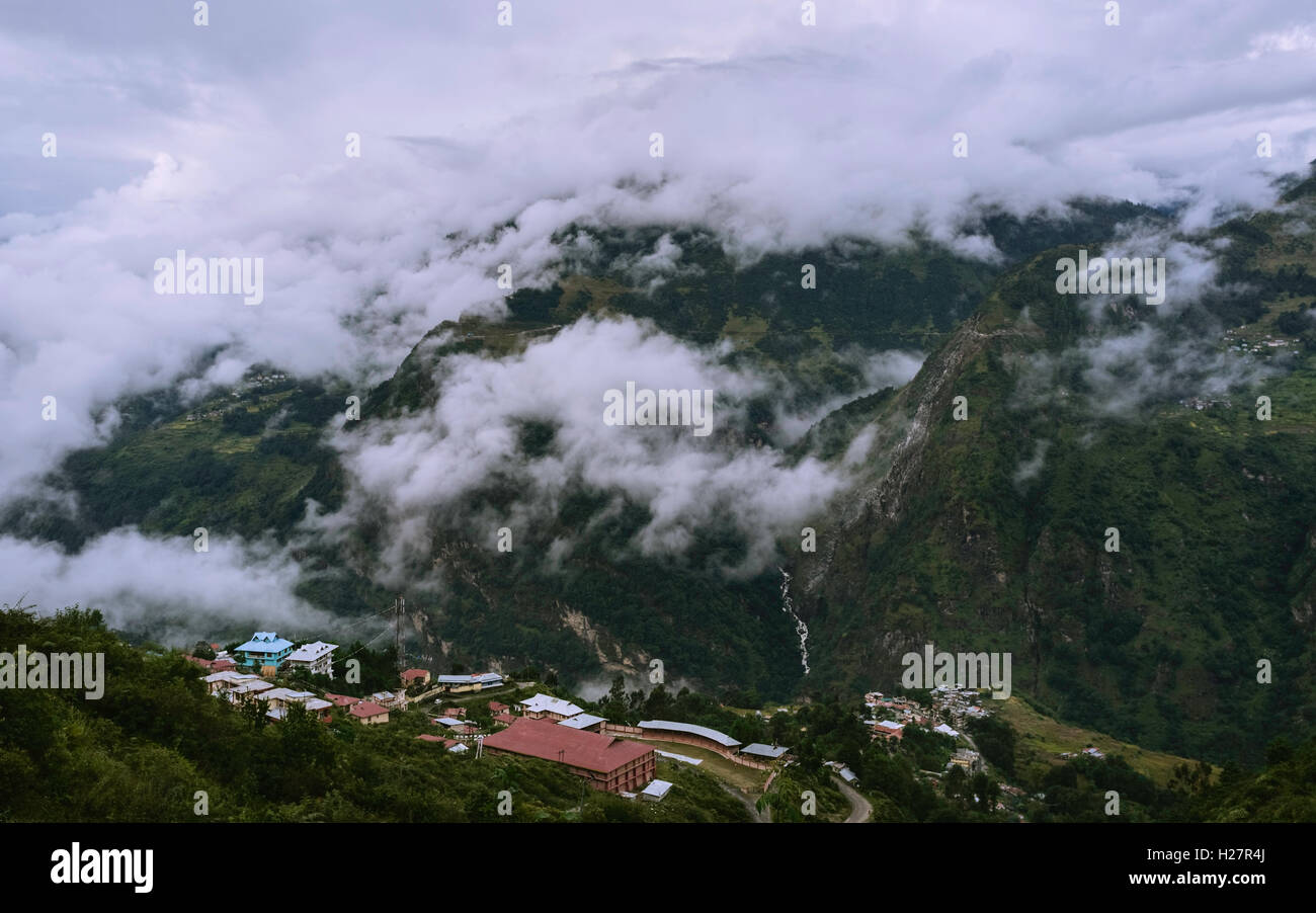 Vista attraverso le alte montagne dell Himalaya in vista di un piccolo insediamento umano all'alba avvolto nella nube, Arunachal Pradesh, India. Foto Stock