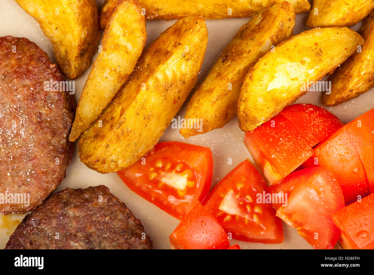 Immagine ravvicinata di hamburger di manzo con cunei di patata e di pomodoro fresco su una piastra Foto Stock