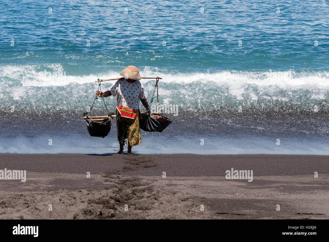 La donna che porta un teku teku-per la raccolta di acqua di mare che in seguito sarà spruzzato sulla sabbia per estrarre il sale. Foto Stock