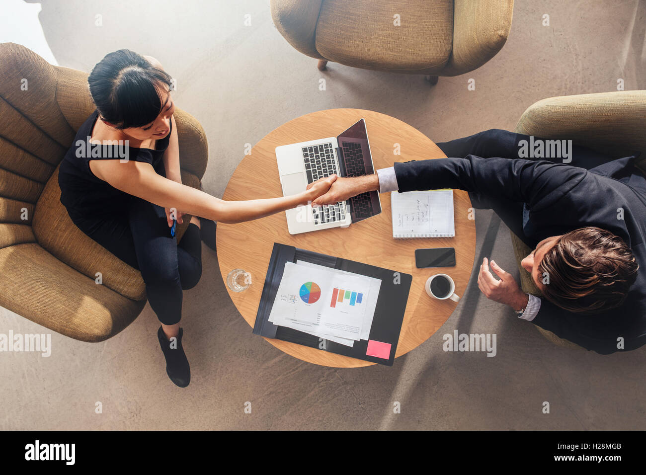 Vista dall'alto di giovani colleghi di lavoro che stringono le mani sulla trattativa. Grafici e laptop sulla tabella che mostra le statistiche e grafici. Foto Stock
