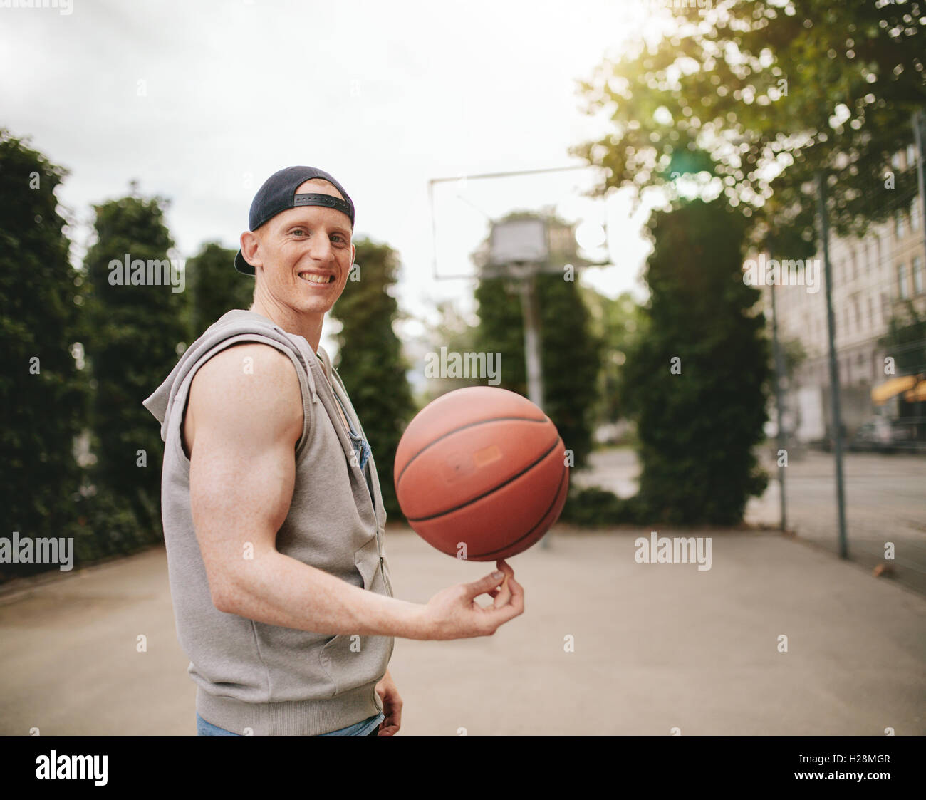 Ritratto di adolescenti streetball player la filatura la palla e sorridente alla fotocamera. Felice giovane uomo di pallacanestro di bilanciamento sulla sua finge Foto Stock