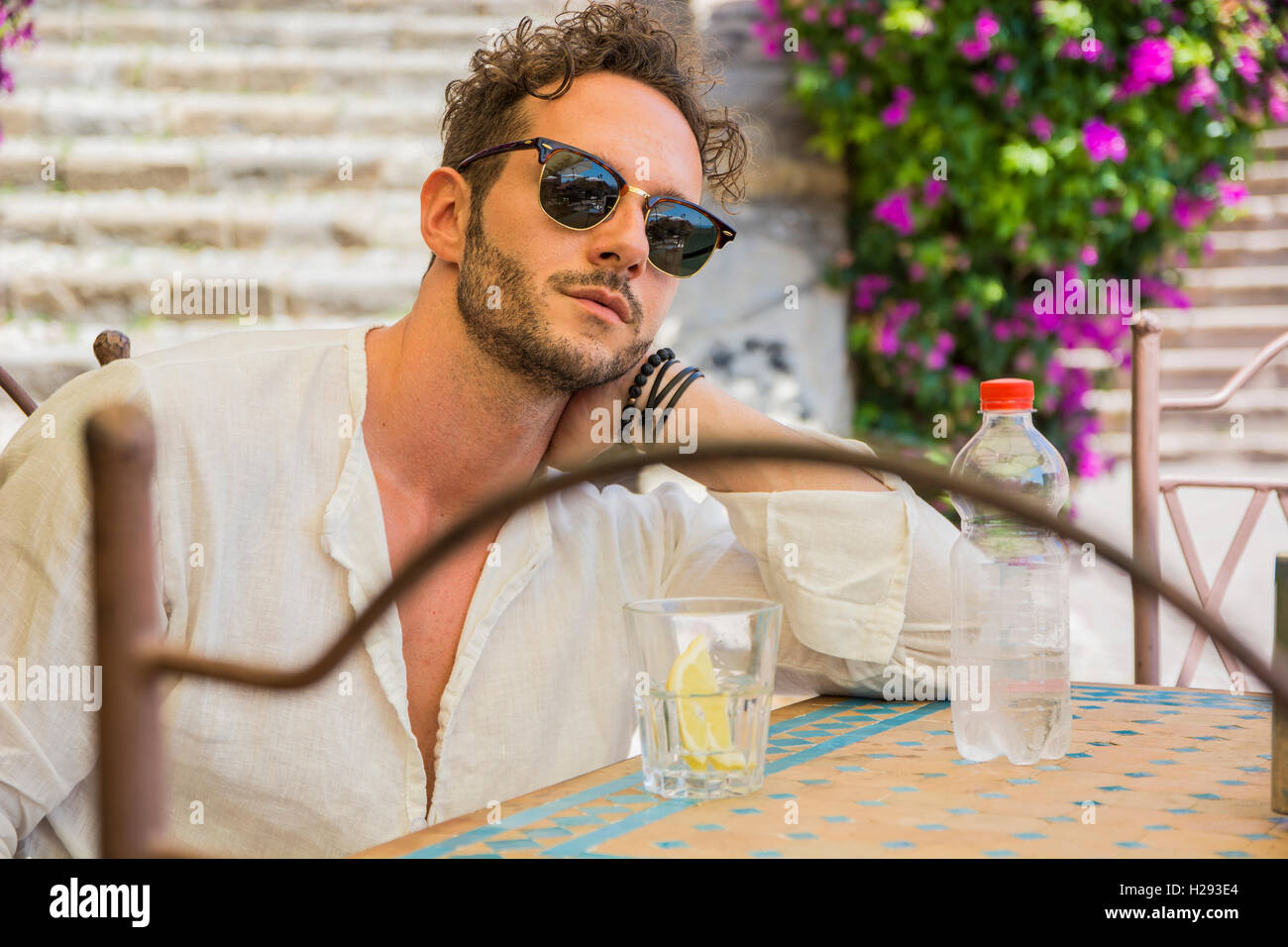 Ritratto di elegante e di buona ricerca uomo in occhiali da sole tenendo una bottiglia di acqua minerale a tavola in cafe Foto Stock