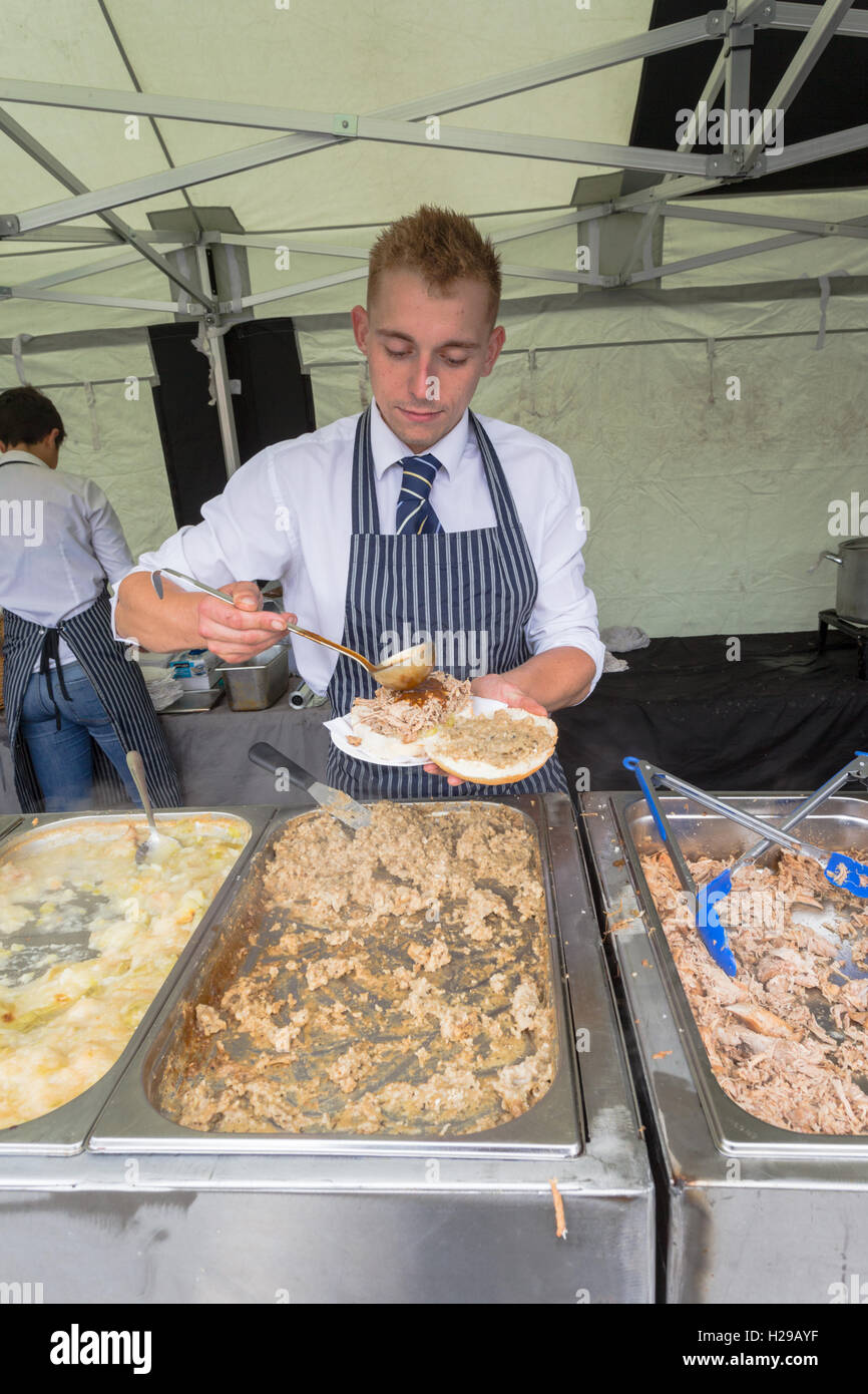 Un giovane uomo che serve un maiale caldi bap o sandwich da un mobile in stallo. Foto Stock