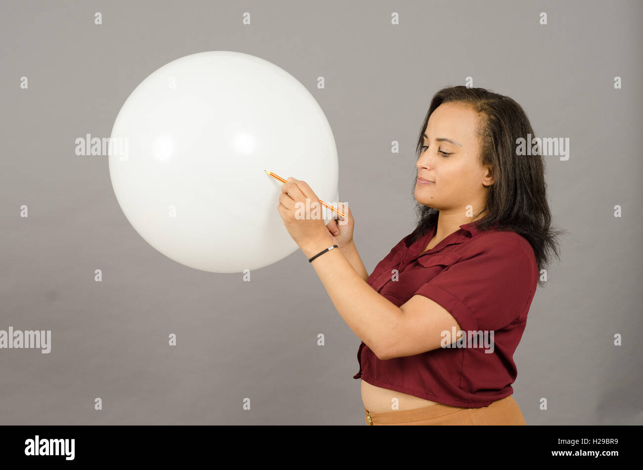 Donna adulta lo scoppio di un grande pallone bianco con una matita. Foto Stock