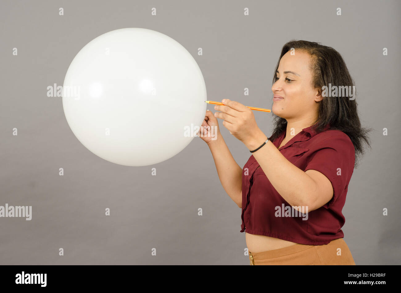 Donna adulta lo scoppio di un grande pallone bianco con una matita. Foto Stock