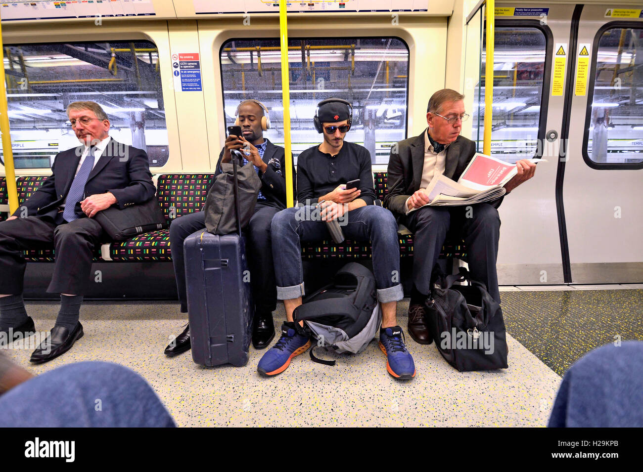 Londra, Inghilterra, Regno Unito. Passeggeri su una Londra metropolitana, treno ascoltando musica / lettura Foto Stock