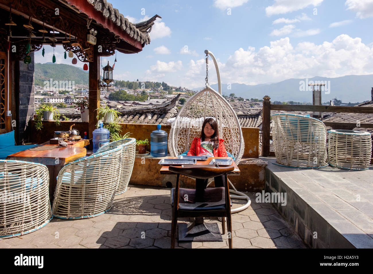 Donna orientale rilassante turistica in poltrona Egg sul patio panoramico con vedute di Lijiang in Cina Foto Stock