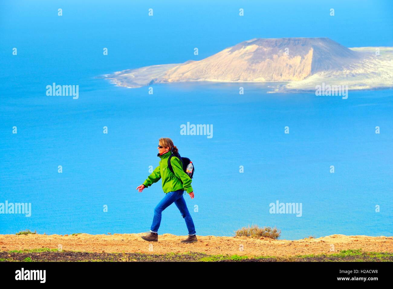 Lanzarote, Isole Canarie. Woman Hiking scogliere sul mare di Risco de Famara a Guinate 550m oltre Atlantico. Isla Graciosa in distanza Foto Stock