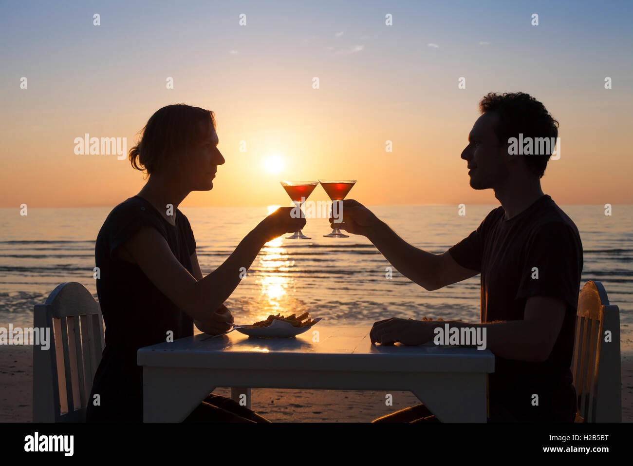 Coppia giovane avente una romantica cena su una spiaggia tropicale con due cocktail Foto Stock