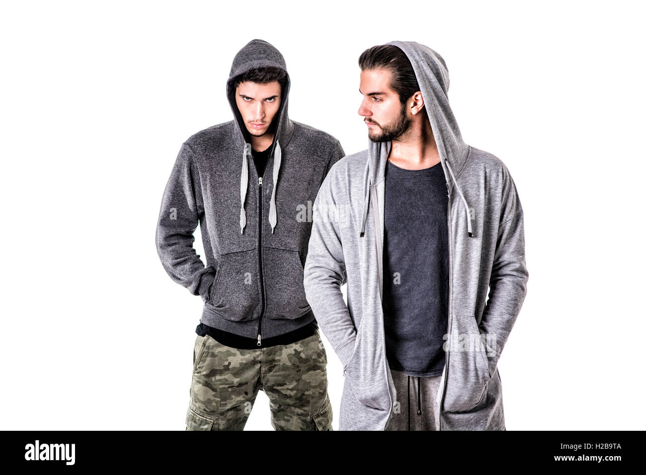 Due giovani uomini che indossano militare e sport vestiti. Cappe da indossare su testate. Studio shot. Foto Stock