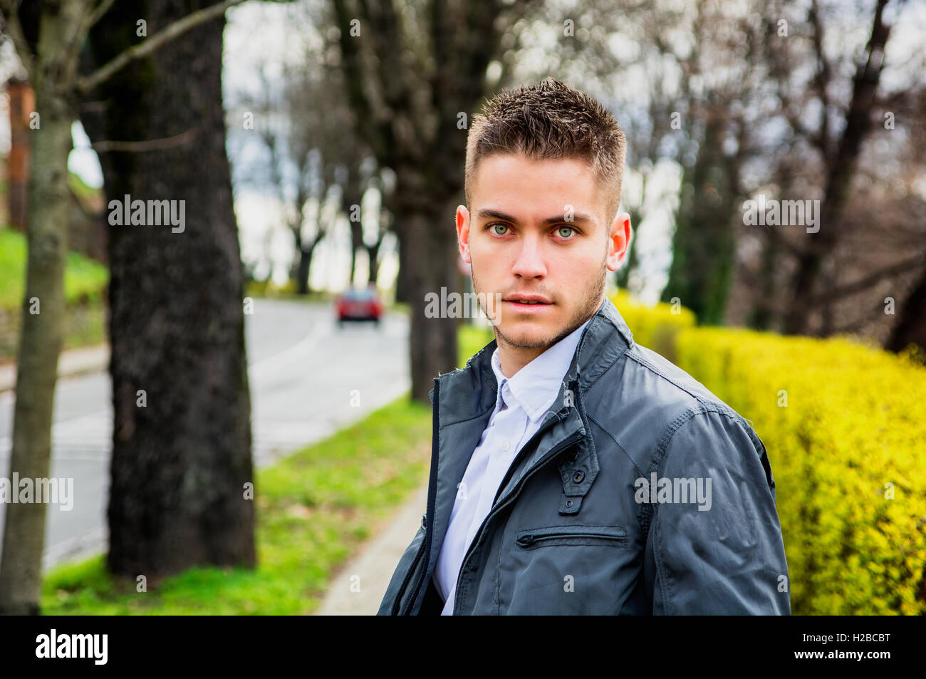 Ritratto di bel giovane uomo in cerca di un lato mentre sedendo nel parco della città Foto Stock