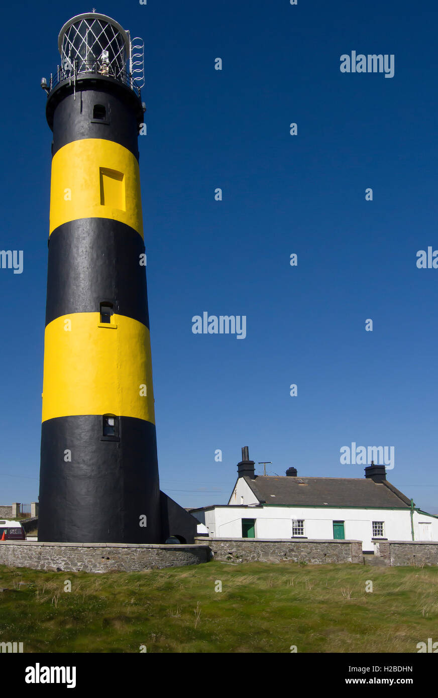 Faro Irlanda con il contrassegno giallo e nero accanto cottage costiero e cielo blu sfondo a St John's Point County in basso Irlanda del Nord Foto Stock